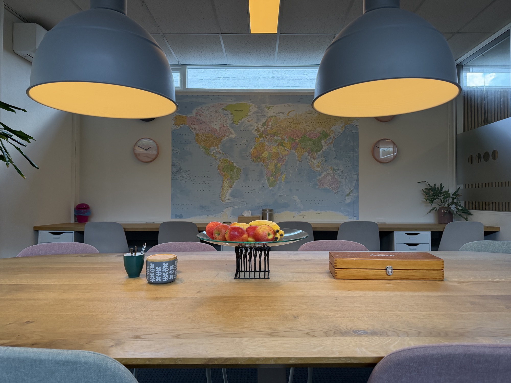 Grote houten werktafel met daarachter een wereldkaart en werkplekken bij Quadraat Zoetermeer